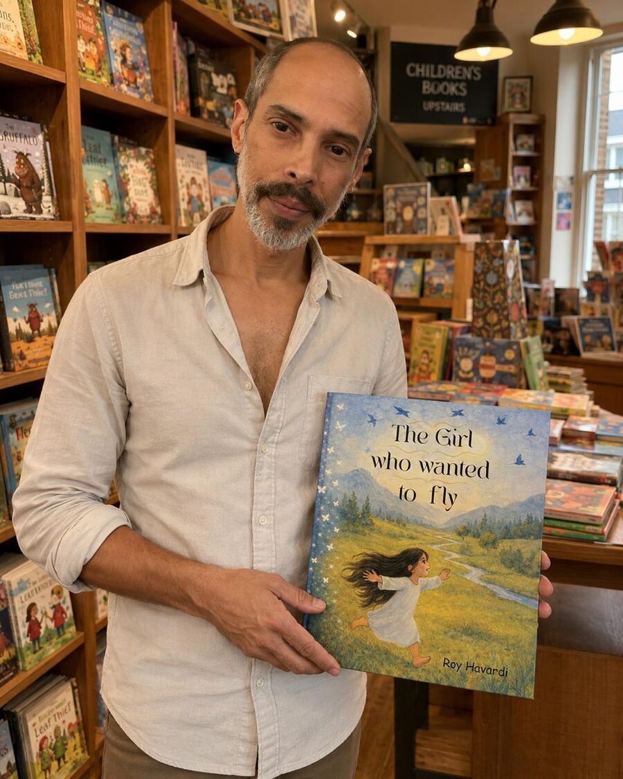 Roy Havardi holding The Girl Who Wanted to Fly in a children's bookshop, shelves of picture books behind him